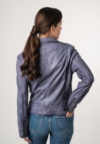 Paarse leren motorjack met een slim fit ontwerp, decoratieve stiksels en ritsmouwen. Draagt met een blauwe jeans.