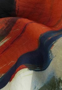 Textil s abstraktními vzory v sytě červené, tmavě modré a zelené barvě. Povrch vypadá hladce s viditelnou texturou štětce.