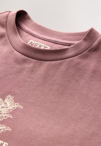Light purple cotton t-shirt with a round neck, featuring an unembellished design and a tag labeled "NEXT." Smooth texture, casual style.