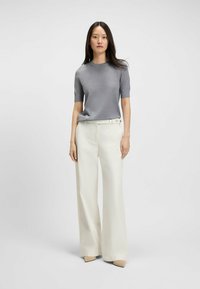 Top corto a maniche corte grigio a maglia abbinato a pantaloni bianchi a gamba larga e tacchi beige. L'outfit presenta un design semplice e linee pulite.
