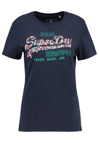 Marinblå bomullströja med färgglad blommig text som säger "Super Dry" och "REAL" i grönt, med ytterligare text nedan i vitt och grönt.