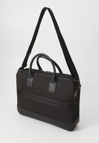 Schwarze Laptop-Tasche mit dualen oberen Griffen und einem abnehmbaren Schultergurt. Verfügt über ein strukturiertes Material und ein geprägtes Logo auf einem Band.