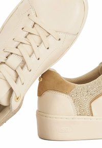 Beige leather sneakers featuring a textured suede accent with embellishments, flat laces, and a rounded toe design.