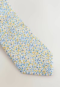 Gemusterte Krawatte mit einem weißen Hintergrund und blauen sowie gelben Blattmotiven, aus einem Stoff mit glatter Textur und spitzem Ende.