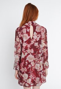 Blumenkleid mit langen Ärmeln, tiefem burgunderrotem Grund, hellrosa und cremefarbenen Blumenmustern, einem Schlüsselloch-Detail am Rücken und Rüschenmanschetten.