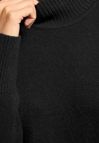 Schwarzer Rollkragenpullover mit gerippter Struktur, Nahaufnahme, die das weiche Material und den gefalteten Kragen mit glatter Oberfläche zeigt.