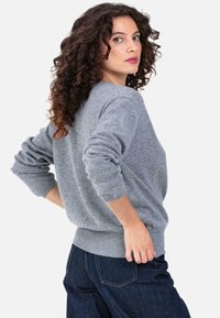 Pull gris tricoté avec un col rond et des poignets côtelés, associé à un jean en denim foncé. La texture semble douce et confortable.