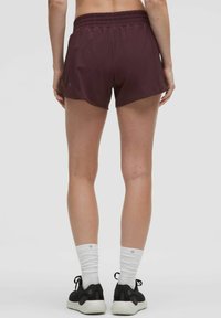 Bordeauxröda atletiska shorts med resårmidja, slät textur och lös passform. Bärs med svarta skor och vita sportstrumpor.