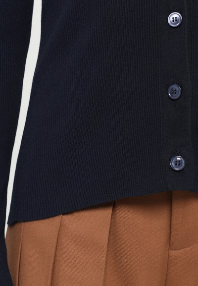 Navy ribbed cardigan with five buttons, featuring a smooth texture and a straight hem, paired with brown pleated fabric below.