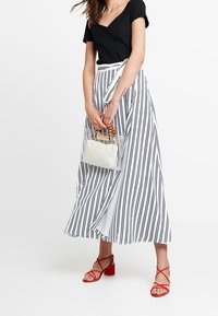 Black short-sleeve top and a white striped maxi skirt. Red strappy sandals. Clear bag with a white interior. Vertical black stripes on skirt.