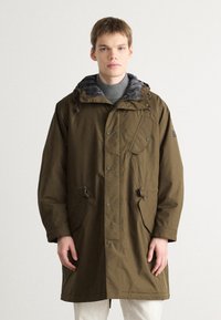 Parka impermeável verde-azeitona com capuz ajustável, forro xadrez, botões de pressão e dois bolsos frontais. Projetada para aquecer e oferecer funcionalidade.