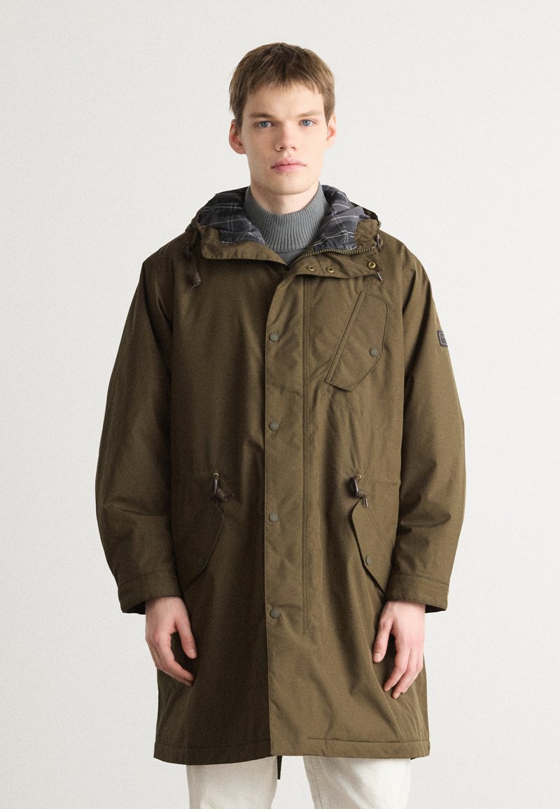 Parka impermeável verde-azeitona com capuz ajustável, forro xadrez, botões de pressão e dois bolsos frontais. Projetada para aquecer e oferecer funcionalidade.