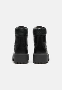 Černé kožené kotníkové boty s texturovaným černým límcem, silnou gumovou podrážkou a detailním prošíváním na těle. Žádné viditelné značení.