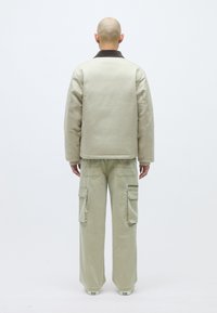 Μπεζ μπουφάν με μόνωση και σκούρο γιακά, σε συνδυασμό με ανοιχτό πράσινο cargo παντελόνι με πολλαπλές τσέπες. Λείος υφασμάτινος χαρακτήρας, χαλαρή εφαρμογή.