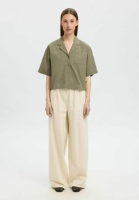 Kratší rukávy, olivově zelená bavlněná button-down košile s kapsou na hrudi, spárovaná s širokými smetanovými kalhotami a černými tkanými botami na podpatku.