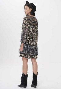 Schwarzes und cremefarbenes gemustertes Kleid mit einem gestuften, gerafften Saum, durchsichtigen schwarzen Ärmeln und einem Spitzenrücken. Kombiniert mit schwarzen Cowboystiefeln und einem Hut.