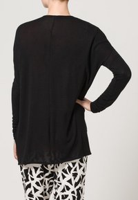Czarna bluzka z długim rękawem o luźnym kroju i zaokrąglonym dole. Lekka tkanina o gładkiej fakturze; z pionowym szwem z tyłu.