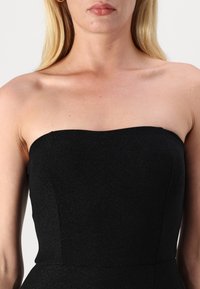 Črna brezramna obleka z oblikovanim korzetom in gladkim materialom, ki se rahlo sveti. Ovratnik je raven in minimalističen.