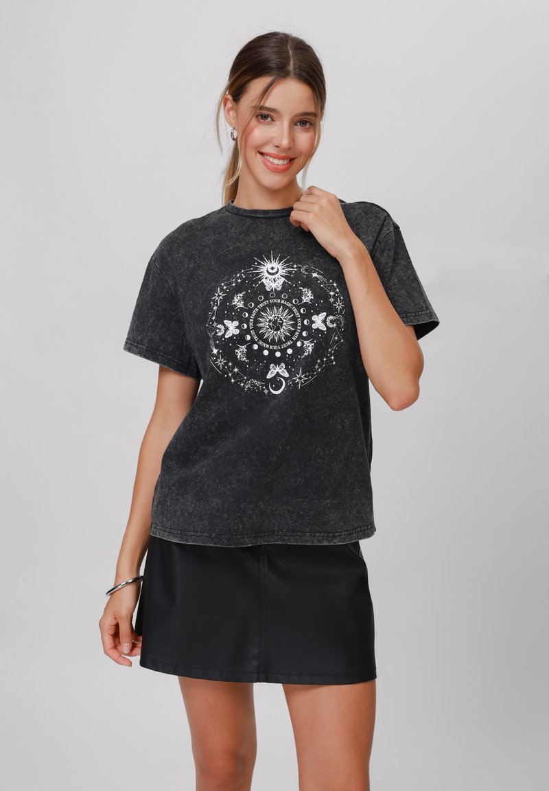 Svart acid-wash t-skjorte med korte ermer, prydet med et hvitt grafisk design av himmellegemer og symboler. Kombinert med et svart miniskjørt.