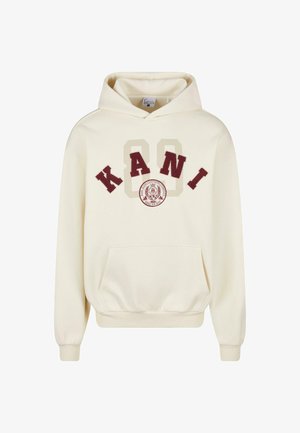 Crème hoodie met "KANI" in bordeauxrood en tan tekst, voorzien van een cirkelvormig embleem boven een kangoeroe pocket en ribgebreide manchetten.