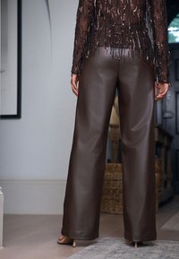 Rjave hlače širokega kroja iz umetnega usnja z gladko teksturo, ki imajo raven kroj in rob. Zadnji pogled prikazuje čiste linije brez žepov.