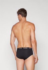 Schwarze Baumwollunterhose mit einem breiten elastischen Bund, der das Puma-Logo zeigt. Einfaches Design, glatte Textur und funktionelle Form.