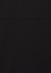 Gros plan sur un tissu noir avec une couture horizontale au centre, montrant la texture et le détail des points.