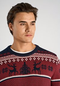 Stickad tröja i vinrött med svarta ren- och snöflingemönster, kompletterad med en marinblå rund halsringning och texturerad design.