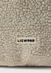 Μπεζ ύφασμα φλις με υφή, αφράτη επιφάνεια. Μια κρεμ ετικέτα διαθέτει το μαύρο κείμενο "LIEWOOD," υποδεικνύοντας την μάρκα.