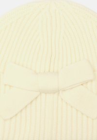 Biała dziana czapka beanie o prążkowanej teksturze z dużą, miękką wstążką z tyłu. Materiał wydaje się ciepły i przytulny.