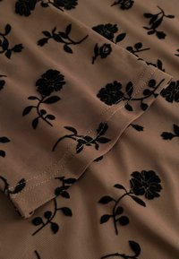 Priesvitná tkanina v svetlo béžovej farbe ozdobená čiernym kvetinovým vyšívaním. Jemné kvetinové vzory zvýrazňujú textúru a detaily dizajnu.