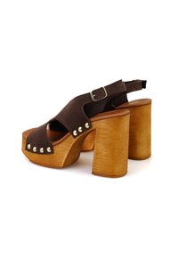 Braune Wildleder-Plateau-Sandalen mit einem dicken Holzabsatz, ausgestattet mit einem Schnallenriemen und metallischen Nieten an der Vorderseite. Strukturierte Holzoberfläche.