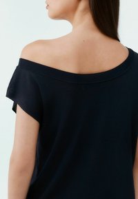 Zwarte off-shoulder top met een relaxed fit, voorzien van een geribbelde halslijn en korte mouwen, gemaakt van een zachte, lichte stof.