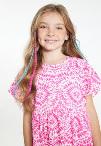 Rožinė marškinėlių su raundiniu iškirpimu ir trumpomis rankovėmis. Plaukai papuošti rožiniais ir mėlynais nertais sruogomis. Šviesus fonas.