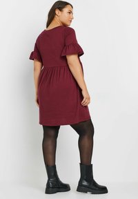 Bordeaux-viininpunainen, lyhythihainen mekko, jossa on röyhelöhihat, kootut vyötärö ja rento istuvuus. Paritettu mustien nilkkurit ja sukkahousujen kanssa. Sileä rakenne.