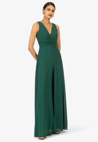 Langes, ärmelloses Kleid aus tiefgrünem Stoff. Es hat einen V-Ausschnitt, eine geraffte Taille, einen fließenden Rock und eine gerade Silhouette.