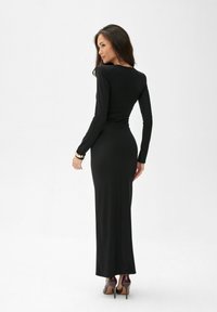 Černé maxi šaty s dlouhým rukávem a přiléhavým střihem, kulatým výstřihem a řasením na zadní straně. Nosené s vínovými lodičkami na vysokém podpatku.