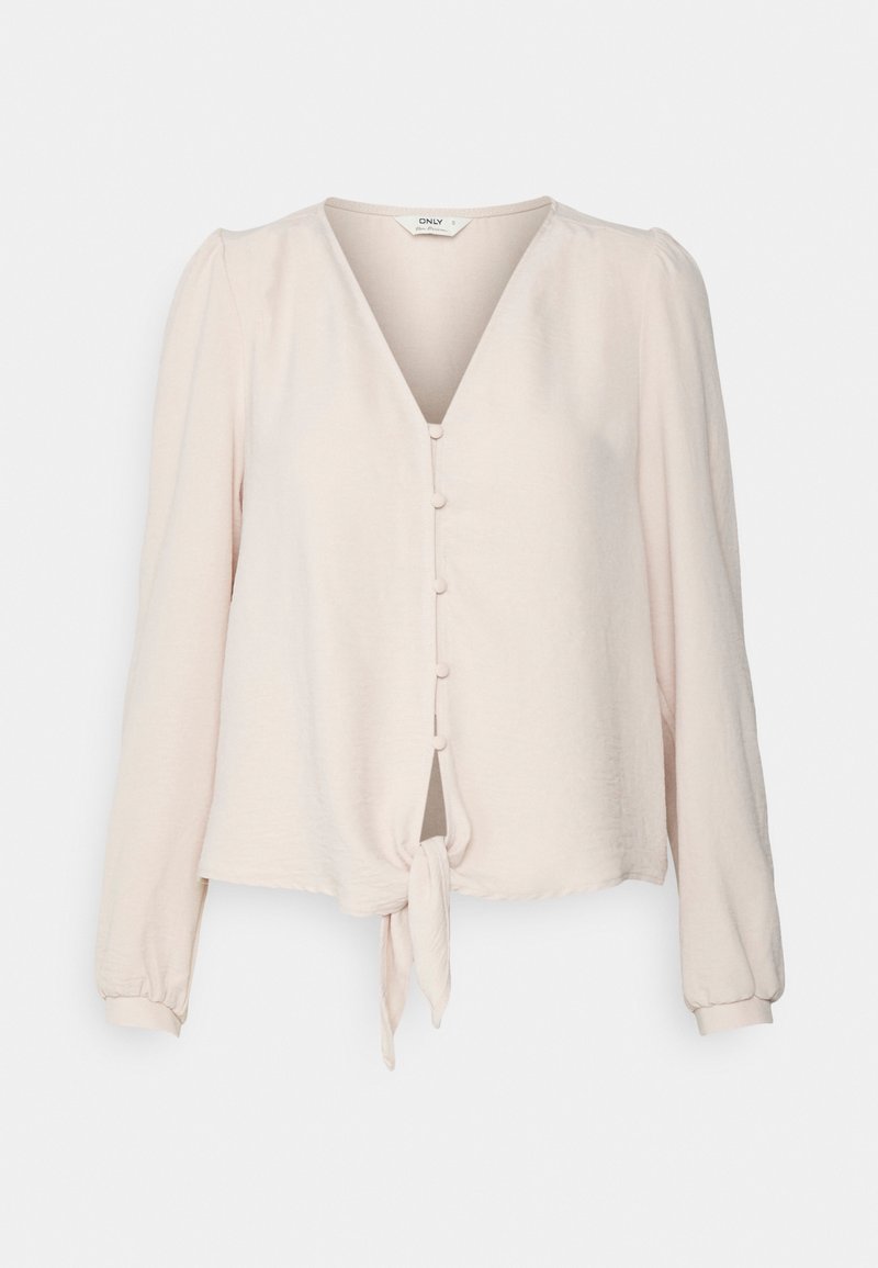 Blouse beige clair à manches longues avec col en V, boutons sur le devant et détail noué à la taille, présentée sur un fond uni.