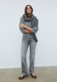 Siv svetr, prekrit z sivim šalom, v kombinaciji z visokimi faded sivimi kavbojkami in superge z živalskim vzorcem. Enostaven in sproščen kroj.