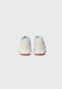 Nike Air sneakers featuring a light beige upper, blue accents on the heel, and a white midsole with a gum rubber outsole.