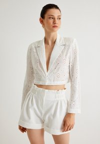 Vit kort jacka med blommönsterbroderi, djup V-ringning och långa ärmar. Matchas med vita högmidjade shorts med rynkad midja.