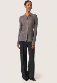 Cárdigan marrón de canalé con cuello, cierre de botones y mangas largas; combinado con pantalones de pierna ancha negros y tacones de punta.
