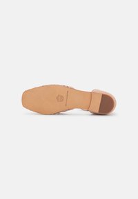 Semelle d'une sandale tissée rose clair avec un bout carré et un petit talon, affichant un logo de marque et un texte sur la semelle en cuir.