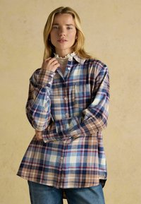 Button-up shirt with a plaid pattern in blue, brown, and cream. Features long sleeves, a collar, and a curved hem. Soft fabric texture.