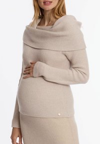 Hellbeige gestreifter Strickpullover mit weitem, schulterfreiem Ausschnitt und langen Ärmeln, ausgestattet mit einem kleinen Akzentknopf an der Hüfte.