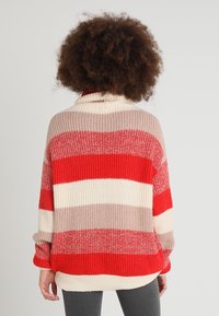 Pull en tricot à col bénitier, présentant des rayures horizontales rouges, crème et beige. Coupe ample avec une texture texturée et un ourlet arrière plus long.