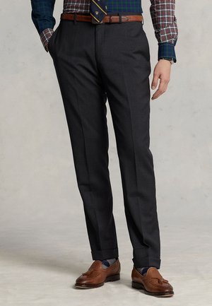 Homme portant un pantalon gris foncé sur mesure avec des revers, des mocassins en cuir marron à glands, des chaussettes à motifs et une chemise à carreaux avec une ceinture et une cravate.