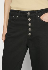 Černé džíny z denimu s pěti knoflíky, stříbrnými dekorativními knoflíky a bočními kapsami. Látka je hladká s mírným elastickým efektem.