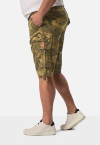 Kamuflage cargo shorts i grønne nuancer, med flere lommer, orange syninger og snørebånd i kanten. Båret med hvide sneakers.