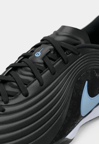 Μαύρο αθλητικό παπούτσι με καμπύλο υφαντό σχέδιο, μαύρες κορδόνες, ανοιχτό μπλε λογότυπο στο πλάι και ένα μικρό ανοιχτό μπλε σύμβολο στη γλώσσα.